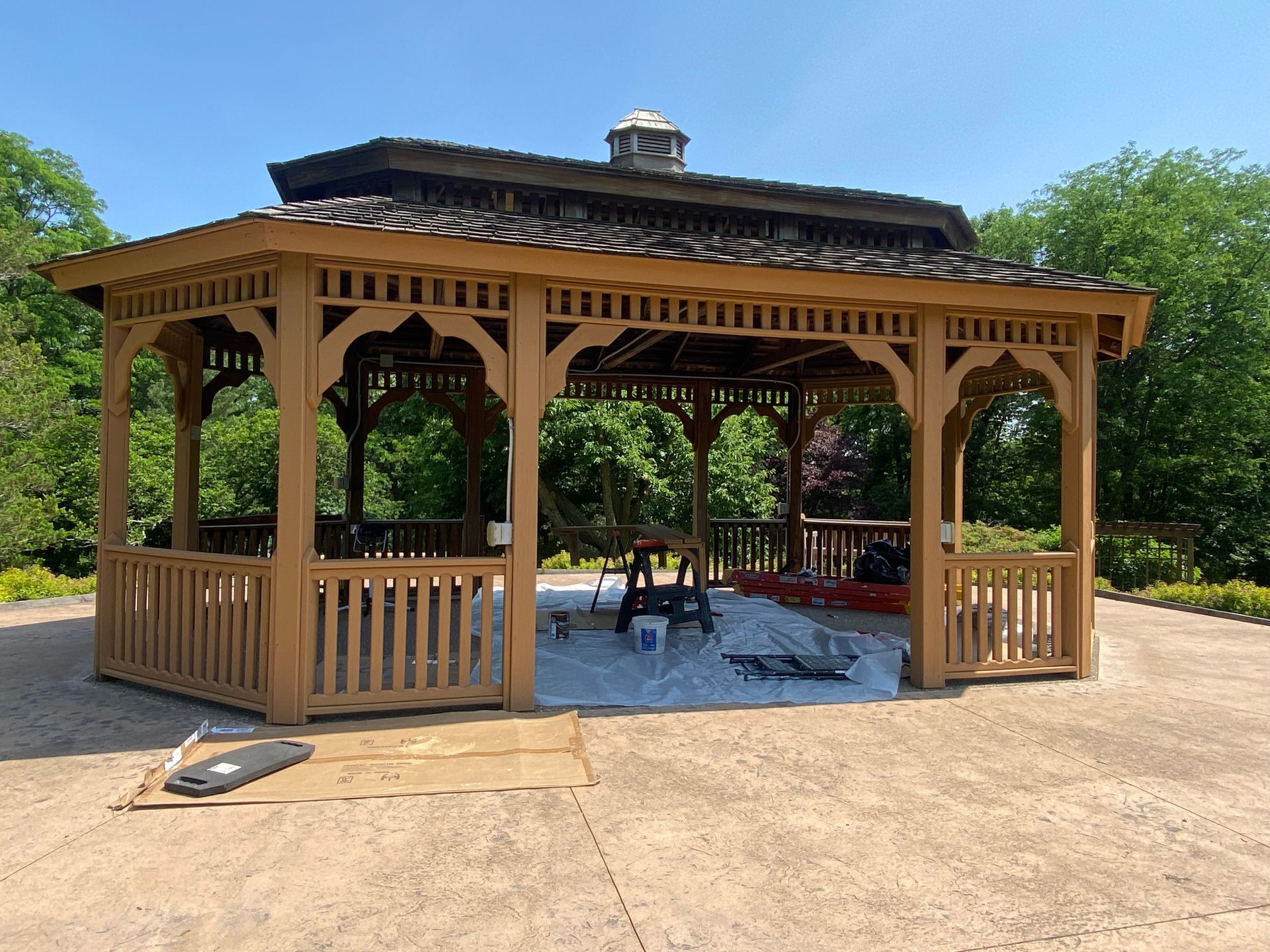 A large wooden gazebo is sitting on top of a concrete driveway.