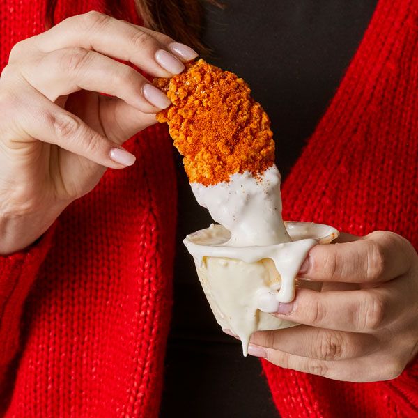 A woman in a red sweater is holding a chicken nugget in her hand.