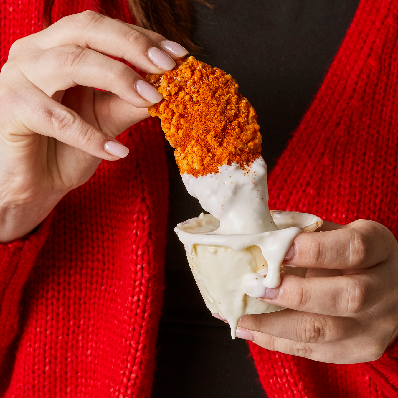 A woman in a red sweater is holding a chicken nugget in her hand.