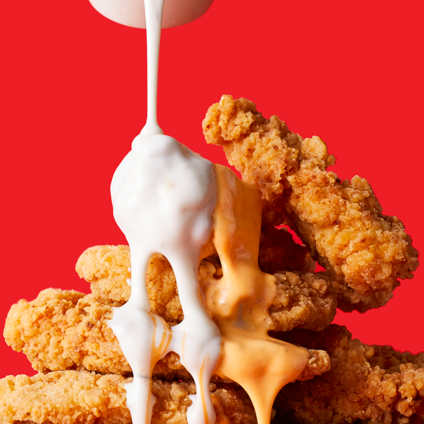 A stack of fried chicken nuggets with sauce being poured on them
