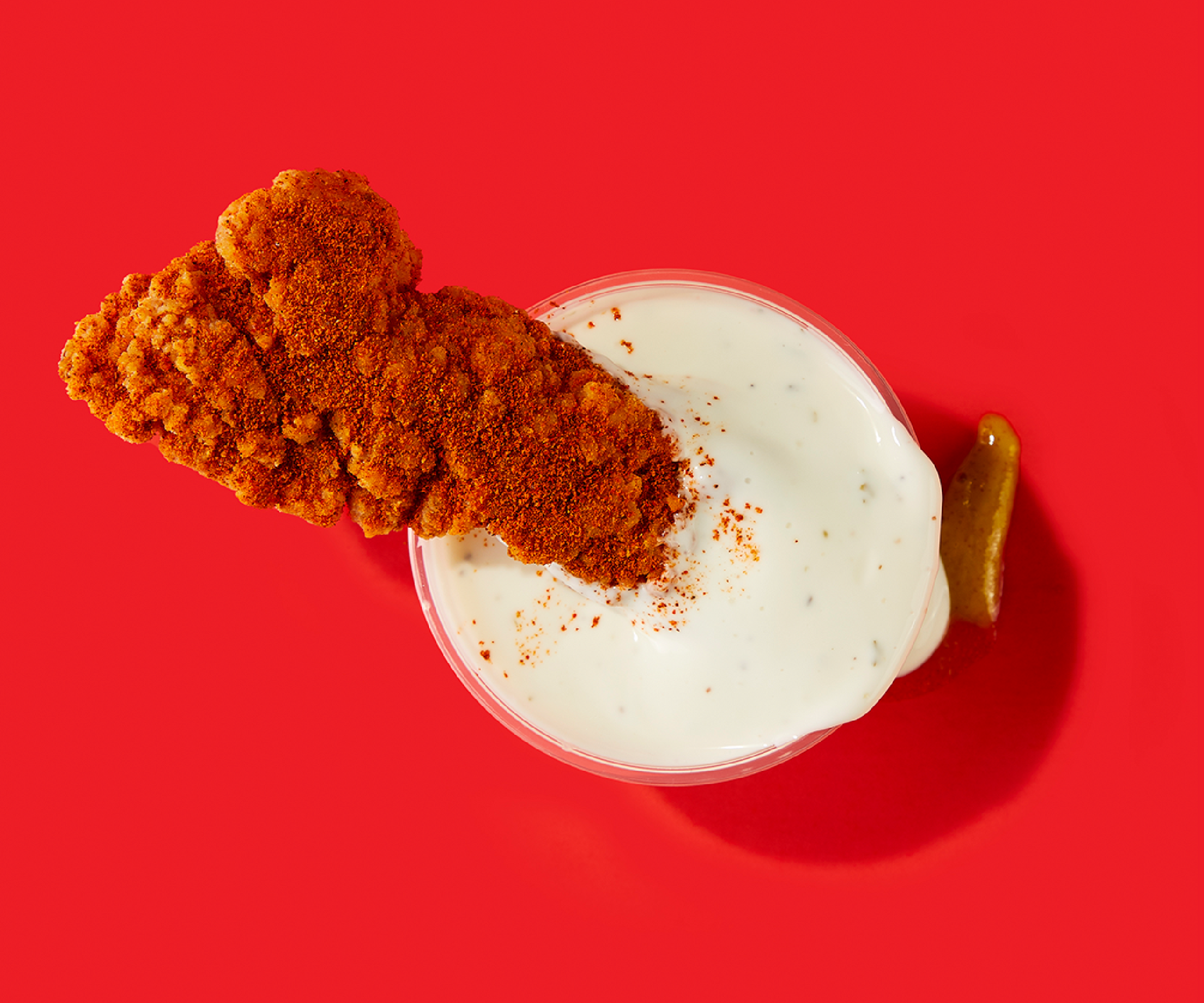 A chicken nugget is sitting on top of a bowl of ranch dressing.