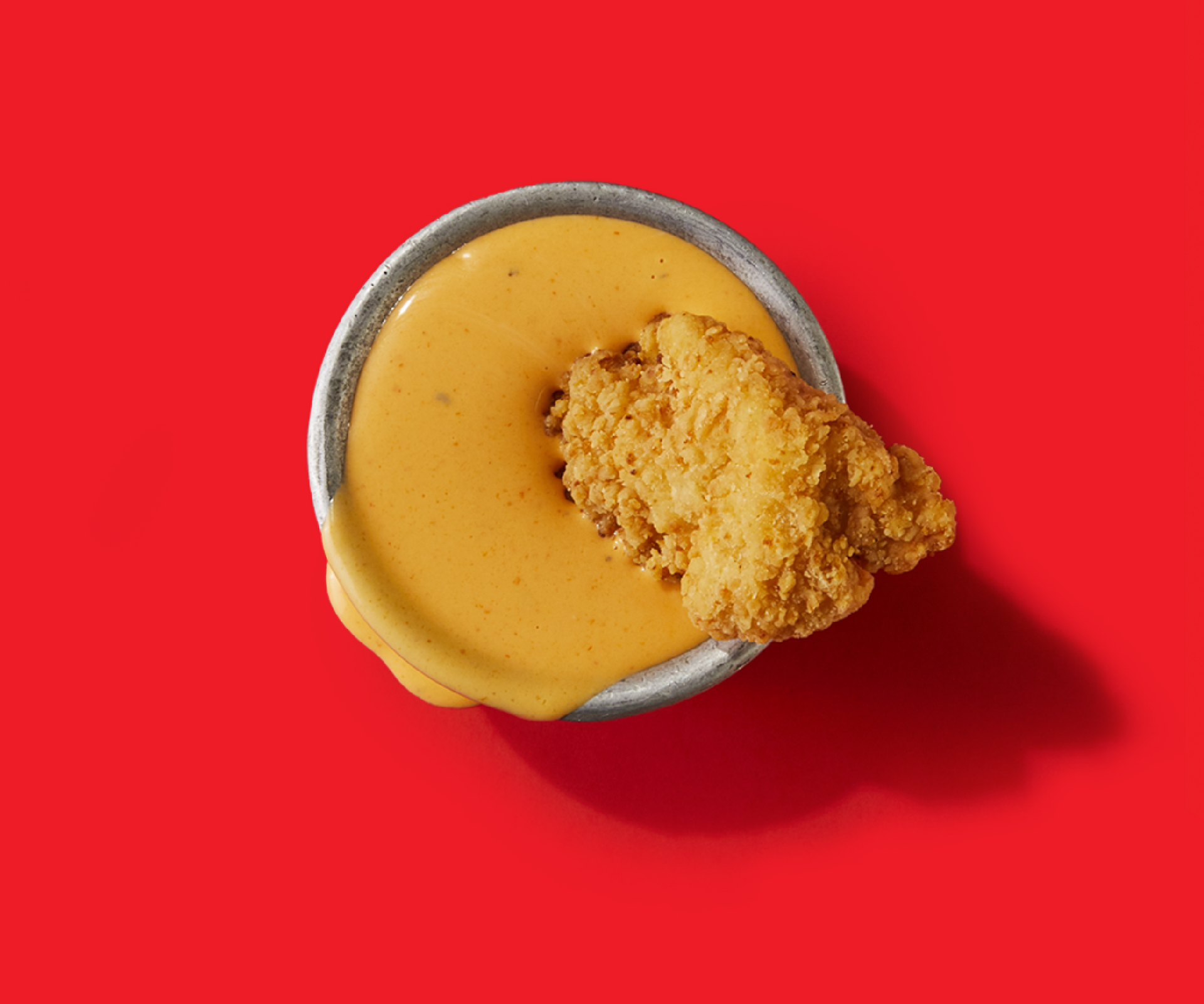 A bowl of cheese sauce with a piece of fried chicken in it.