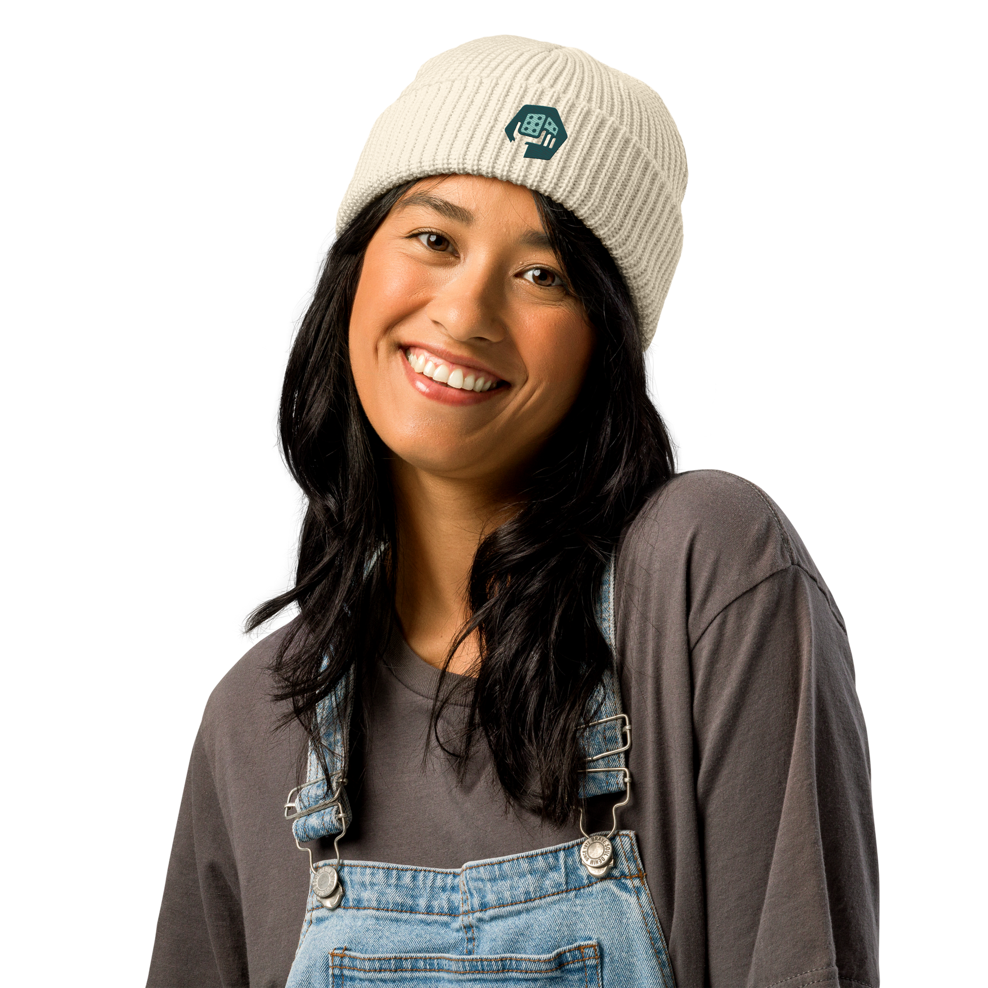 Woman wearing a cream beanie with a logo, smiling, wearing gray shirt and blue overalls.