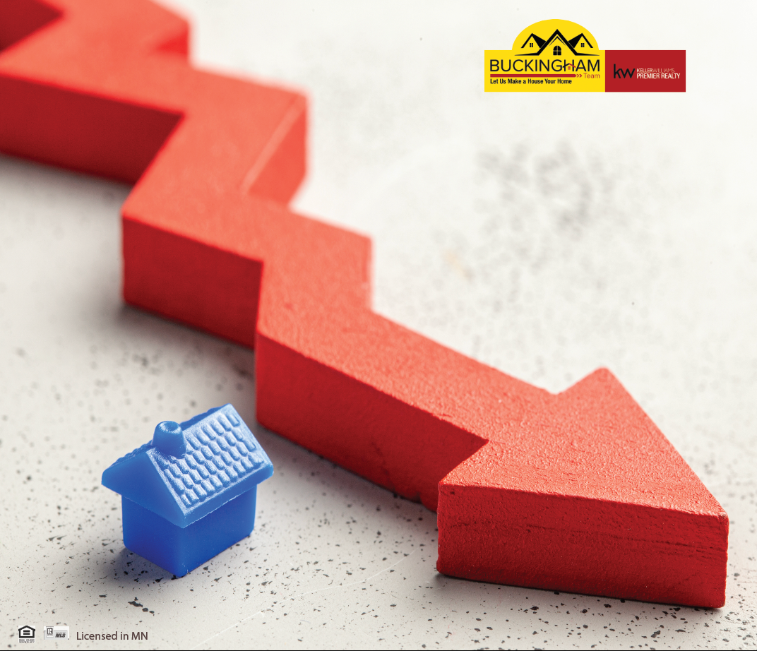 A red downward arrow pointing toward a small blue house, symbolizing declining real estate prices.