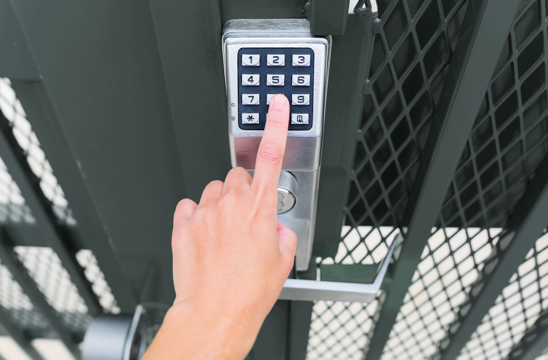 A person pressing a button on a metal gate, indicating an action to open or unlock the gate