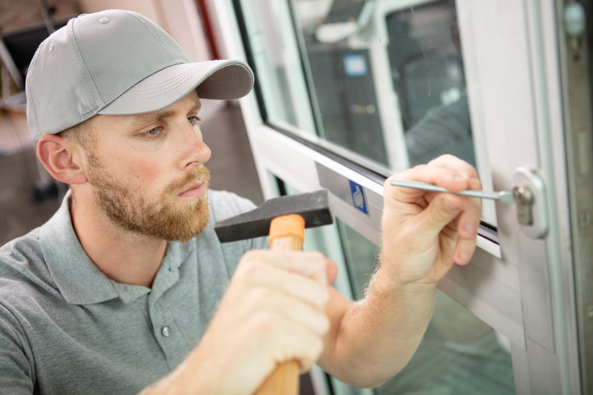 A locksmith repairs a commercial door using a hammer, focused on his task in a well-lit environment A locksmith repairs a commercial door using a hammer, focused on his task in a well-lit environment