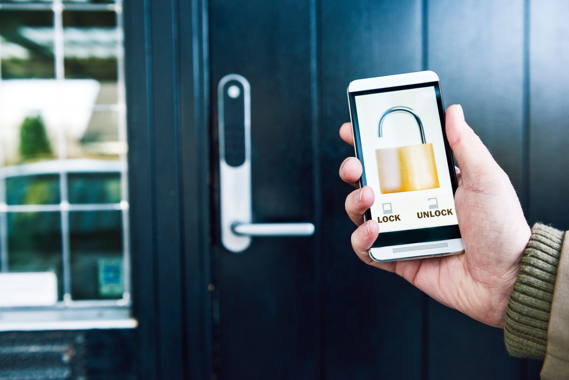 Hand unlocking a door with a smartphone app; black door, silver handle, and a glimpse of a window.