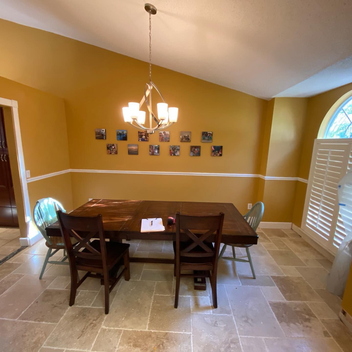 Dining room with large wooden table, chairs, chandelier, and yellow walls with white trim.