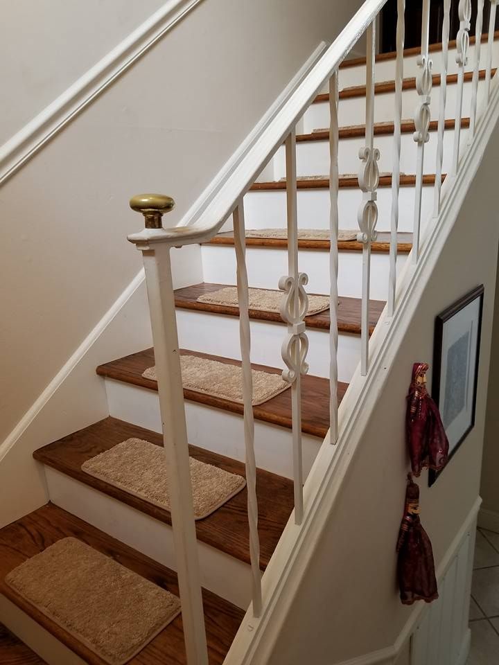 Staircase with white railing, wood steps, beige carpet runner, and decorative tassels on the banister.