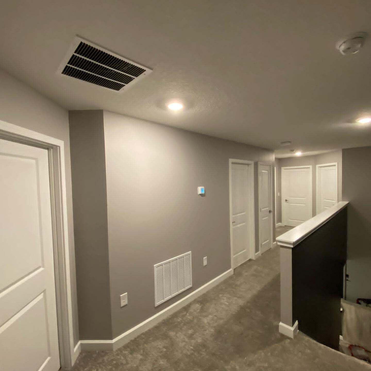 Hallway with gray walls, white doors, ceiling vents, and recessed lights beside a staircase railing