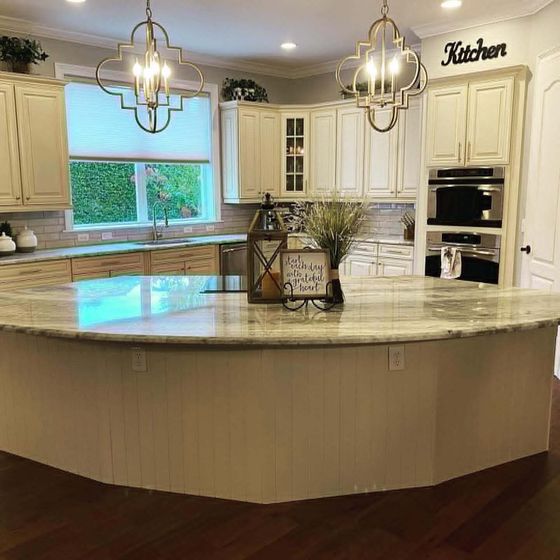 Bright white kitchen with large curved island, pendant lights, and built-in oven.