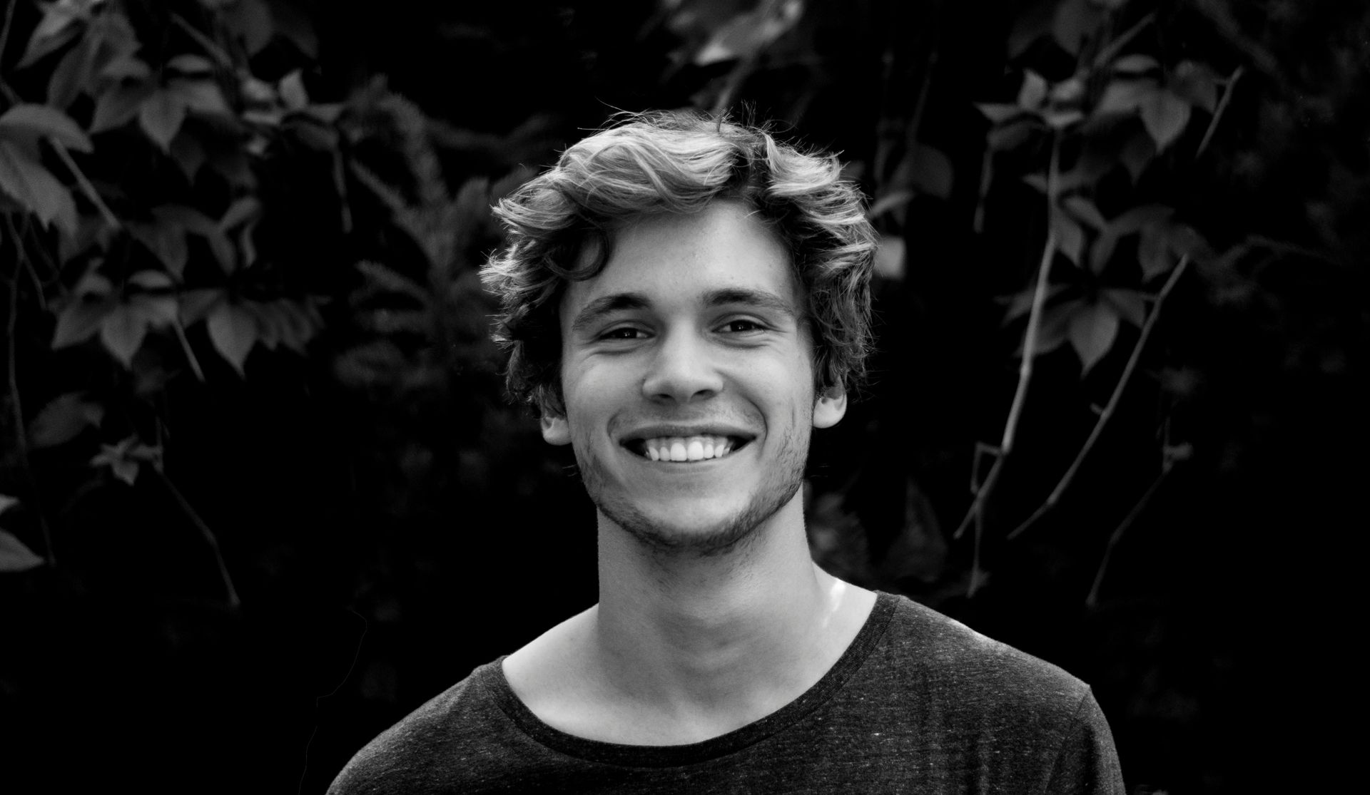 Smiling person in front of dark leafy background.