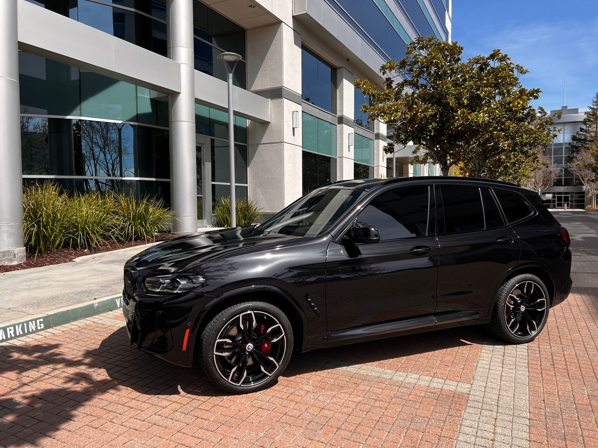 Black SUV parked on a brick path beside a modern building in daylight