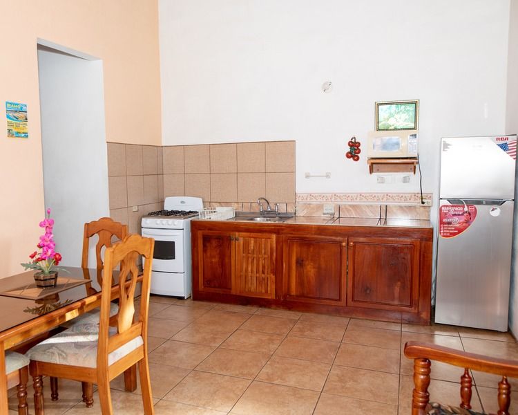 Small kitchen with wooden cabinets, stove, refrigerator, tiled floor, and a dining chair