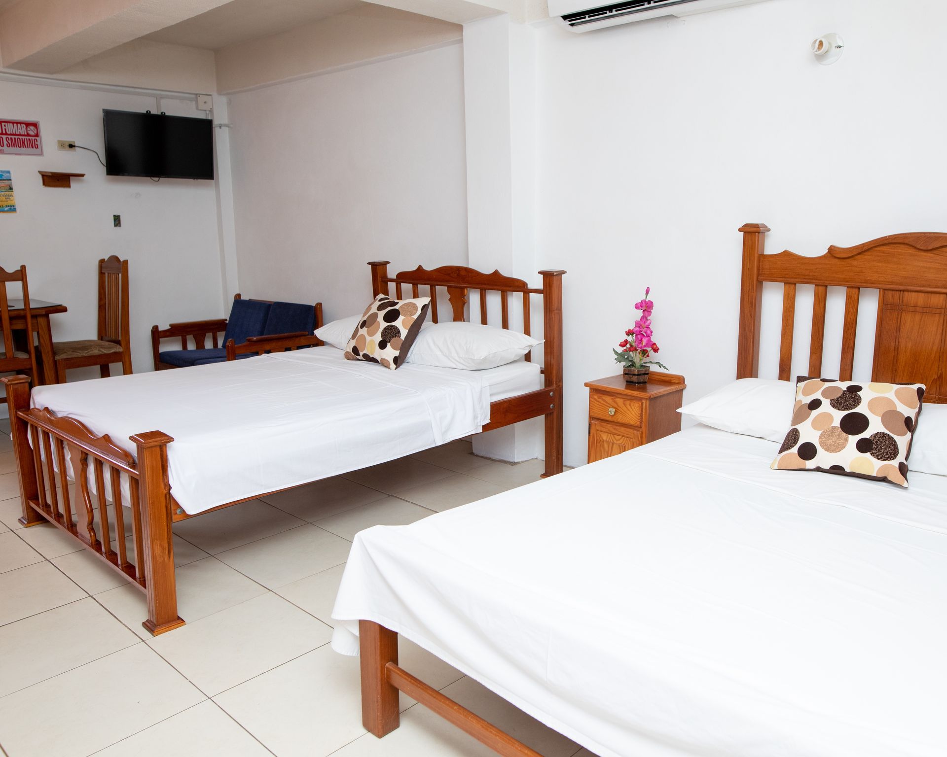 Bright hotel room with two wooden beds, white linens, and a small nightstand between them.
