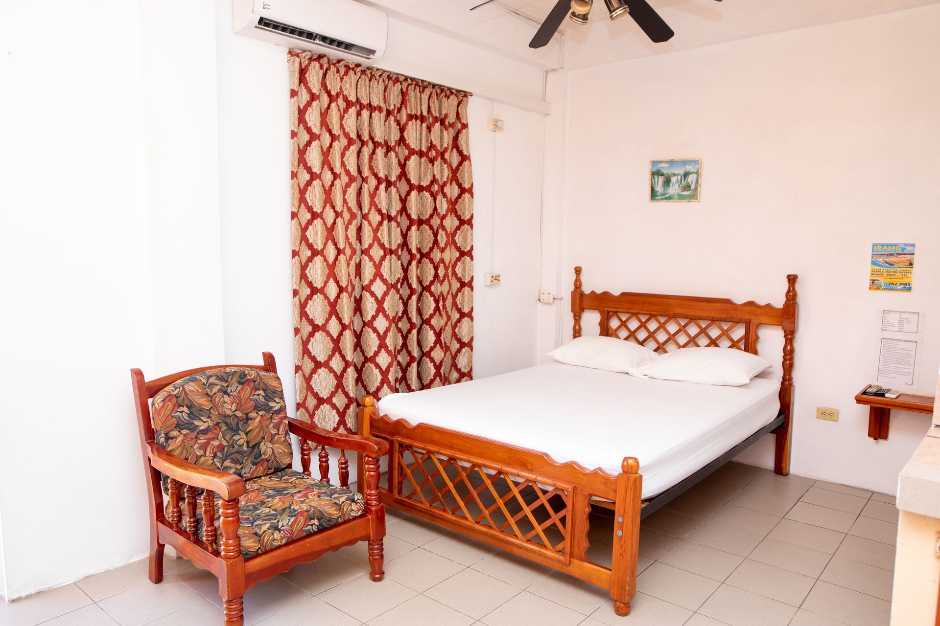 Simple bedroom with carved wooden bed, patterned curtains, and floral armchair