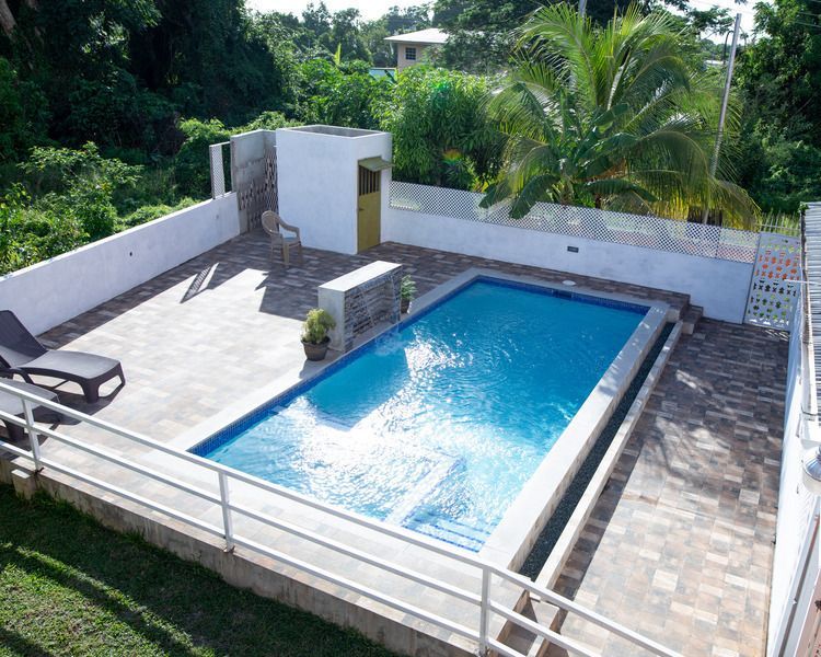 Outdoor rooftop pool with blue water, white walls, lounge chair, and surrounding greenery
