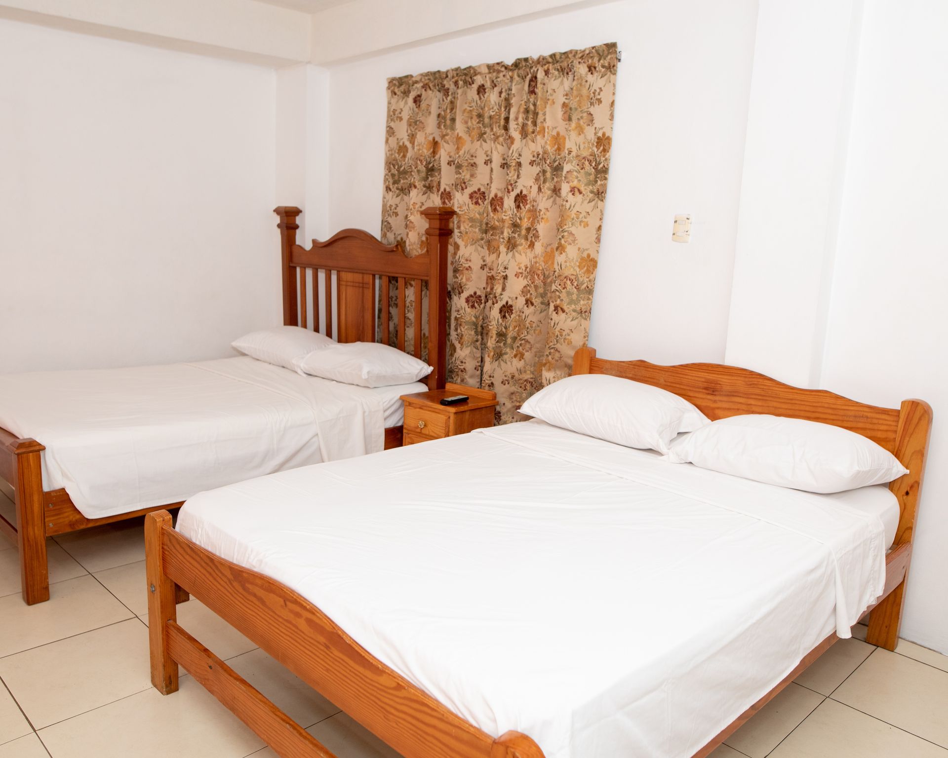 Small bedroom with two wooden beds, white bedding, and a patterned curtain.