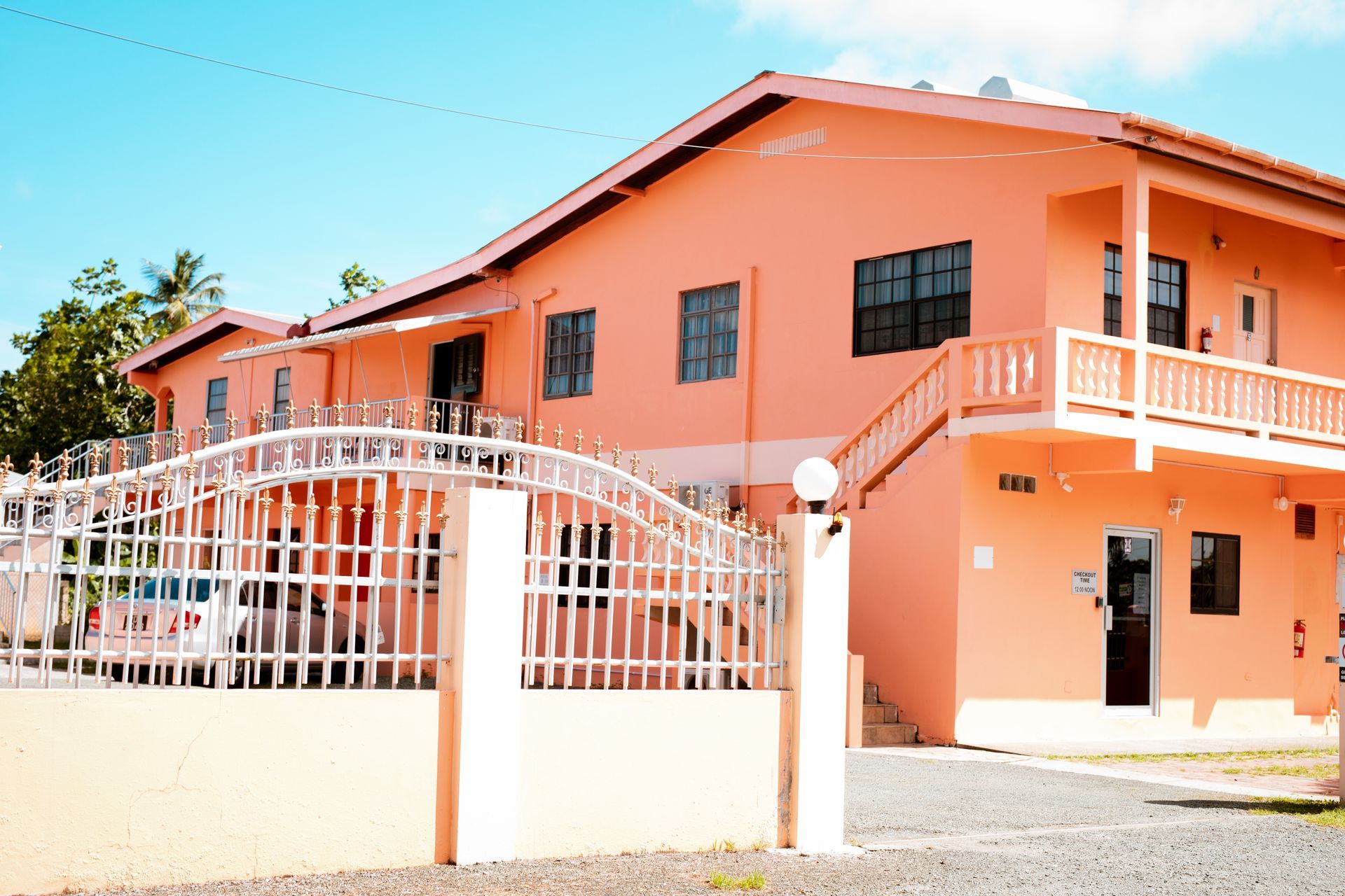 Orange two-story house with white gate and balcony in a sunny residential area