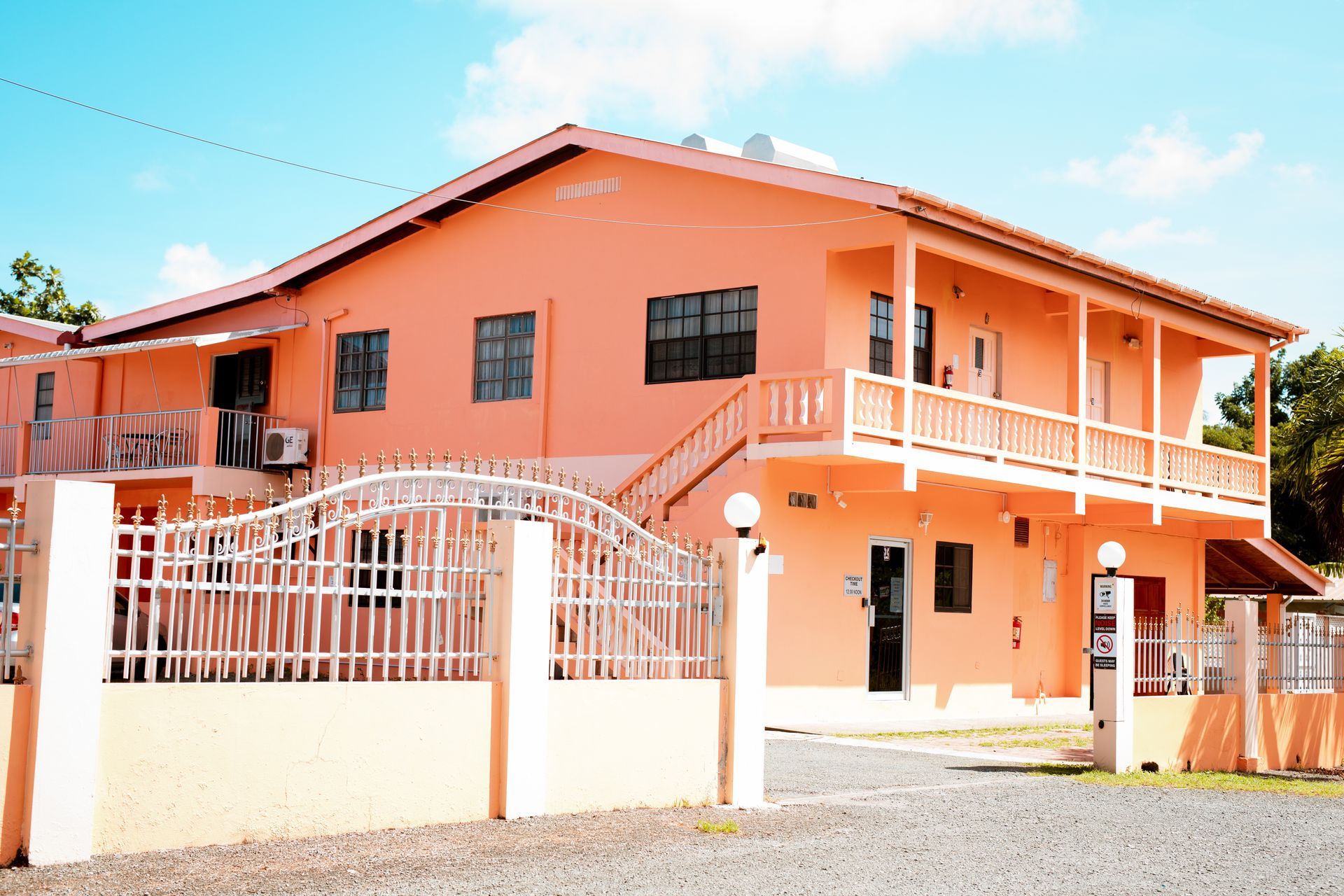 Orange two-story house with balcony, white trim, and a fenced front yard under a clear sky