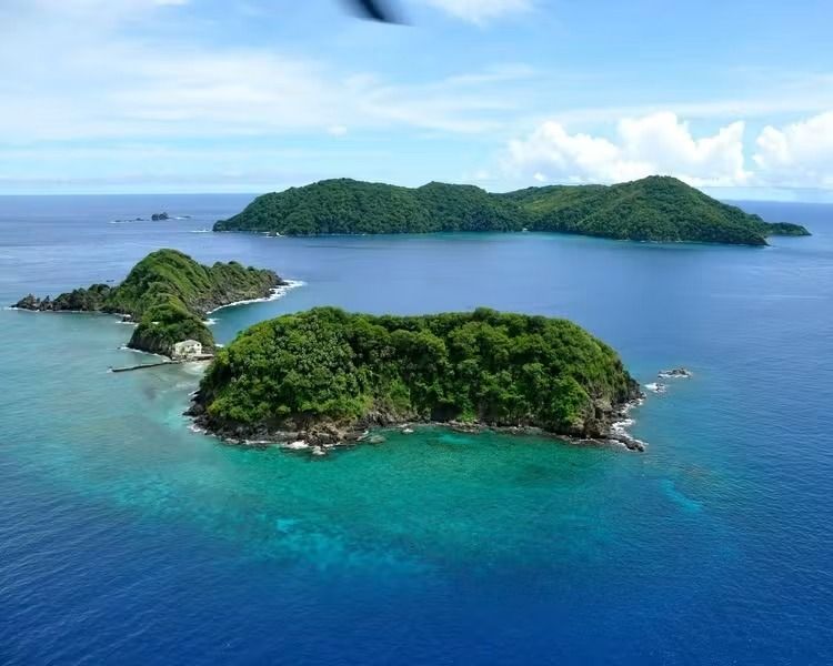 Aerial view of lush green tropical islands in a blue ocean with clear turquoise shallows