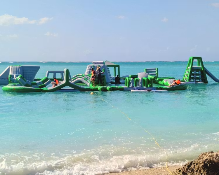 Floating inflatable obstacle course on calm turquoise ocean near a sandy beach under a clear sky