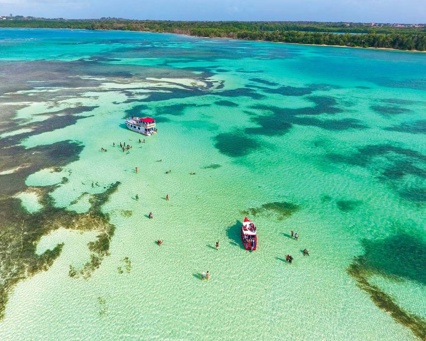 Aerial view of turquoise shallow water with two small boats near a coral reef