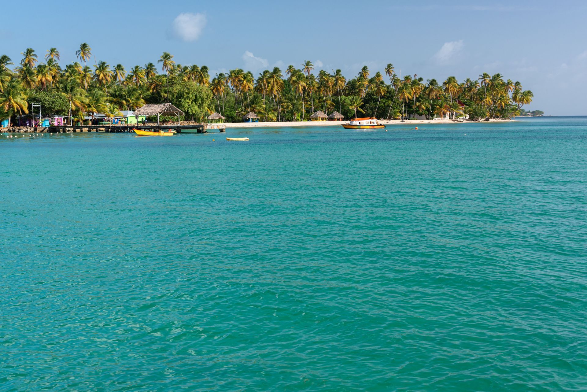 Turquoise tropical bay with palm-lined shore and boats in the distance