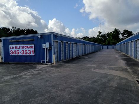 Blue self-storage units along a paved lane under a partly cloudy sky.