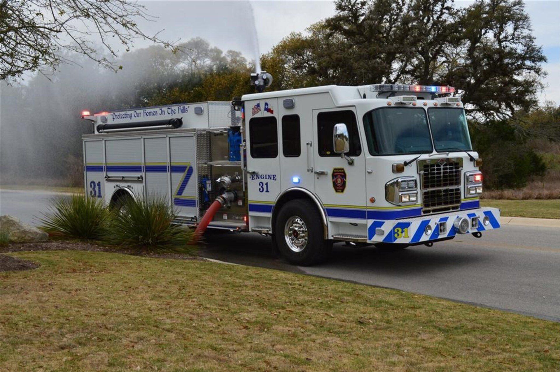 A white and blue Bergheim VFD fire truck is spraying water from the top deck gun.