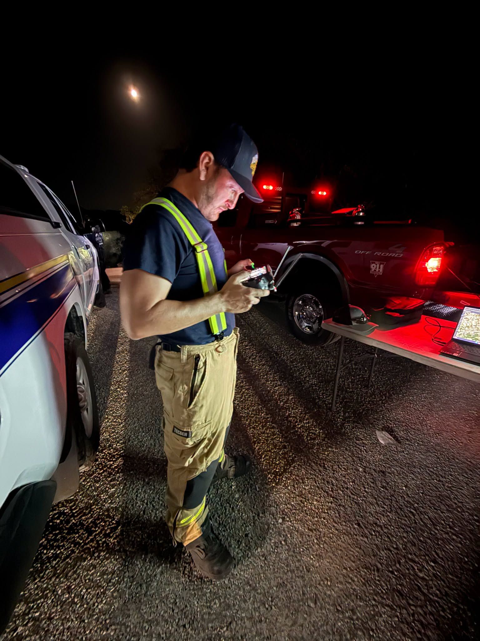 Firefighter in reflective gear checking a phone beside emergency vehicles at night