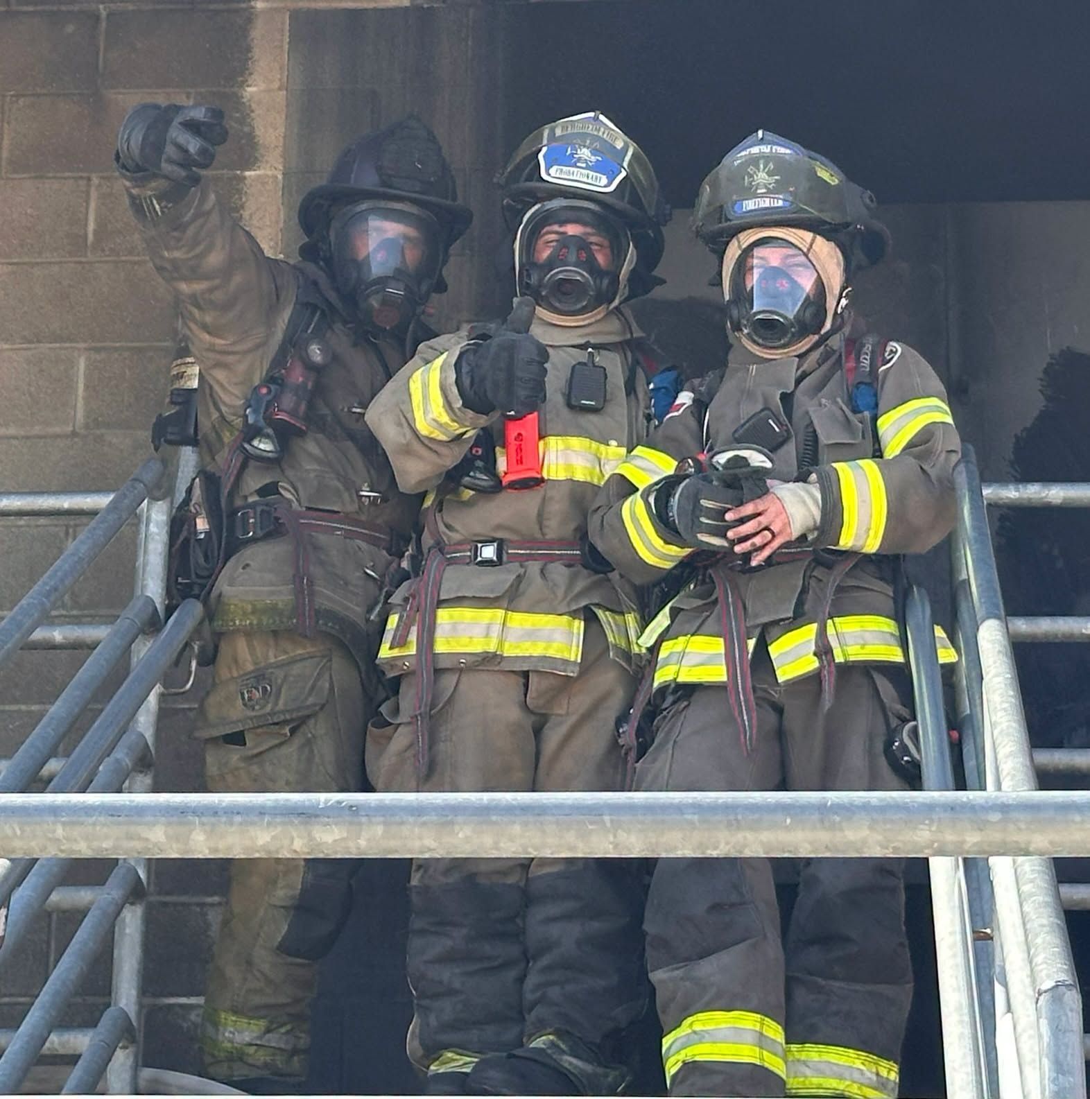 Three firefighters in gear standing on a smoky balcony, one raising a fist.