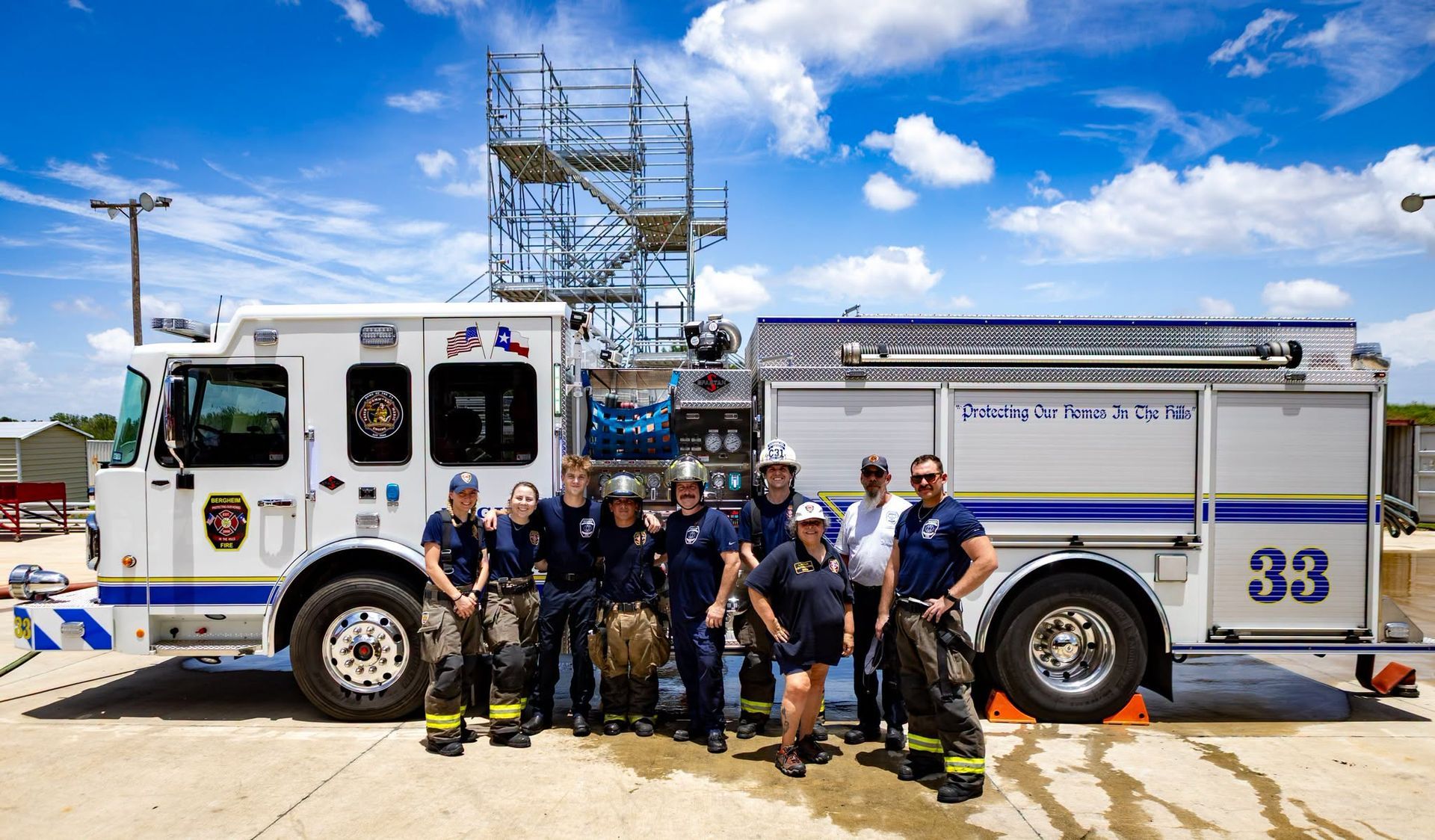 Fire truck with firefighters posing in front of it at a sunny industrial site