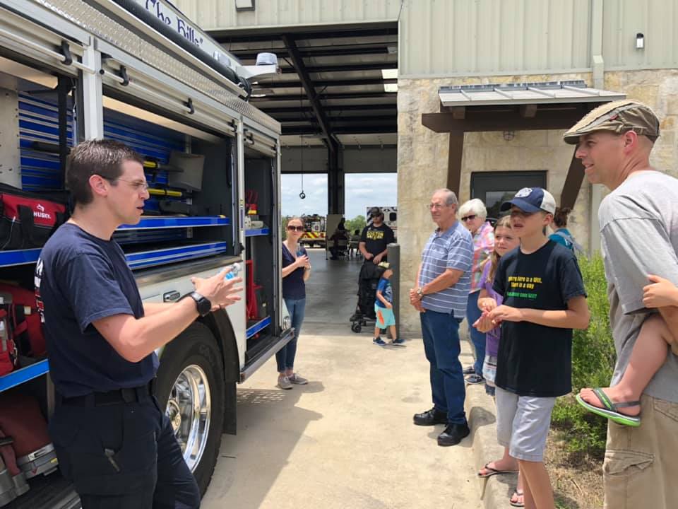 A fire fighter is talking to a group of people in front of a fire truck.