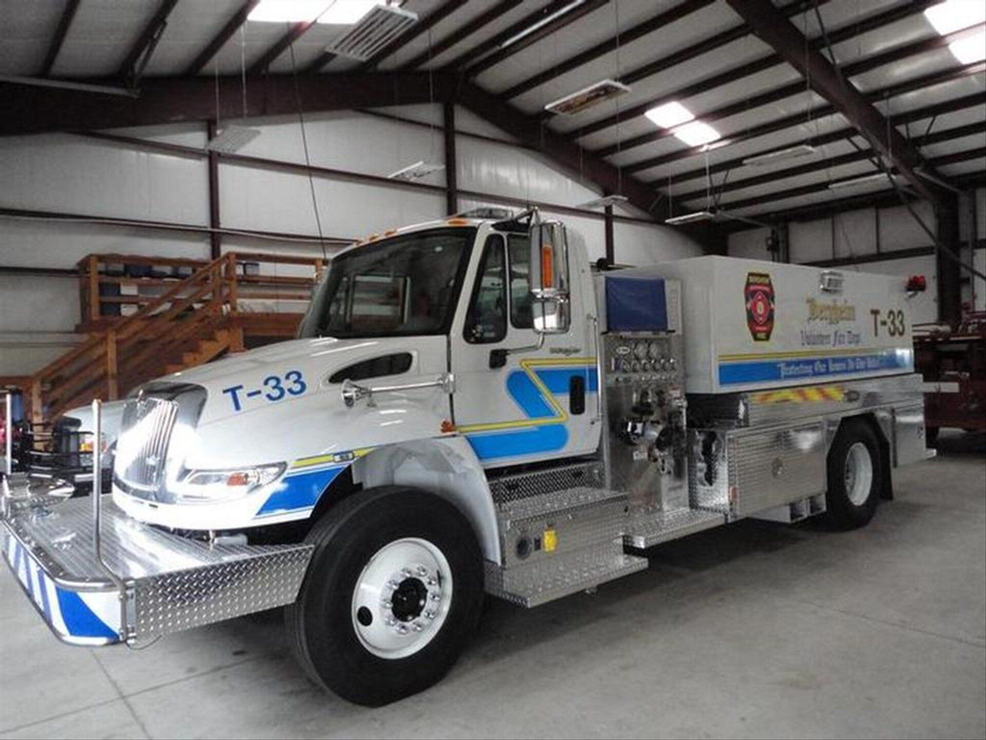 A white and blue Bergheim VFD fire truck  with the number t-33 on it is parked in a fire station.