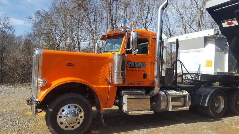 Orange semi truck with white dump trailer parked outdoors on a gravel lot