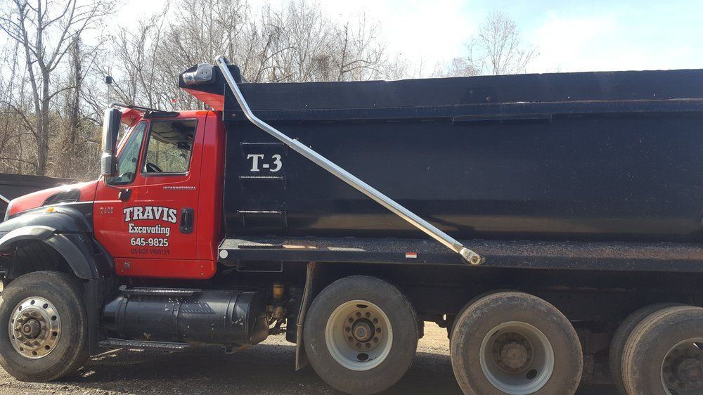 Red dump truck with black trailer and T-3 marking parked outdoors near bare trees