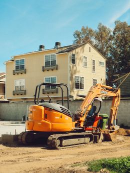 Orange excavator at a construction site beside a beige apartment building on a sunny day