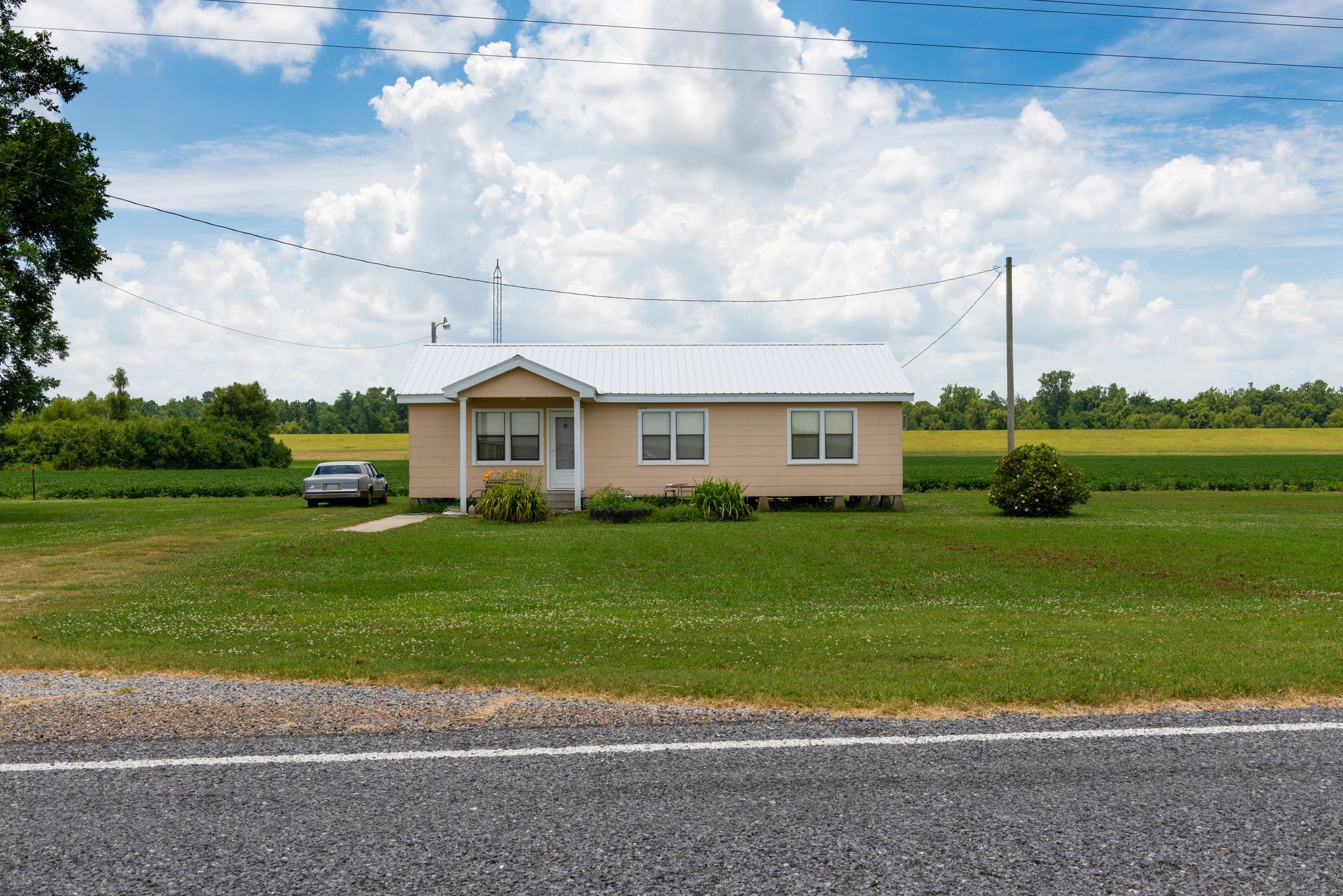 Single-story beige house with a green roof on a wide grassy lot under a partly cloudy sky