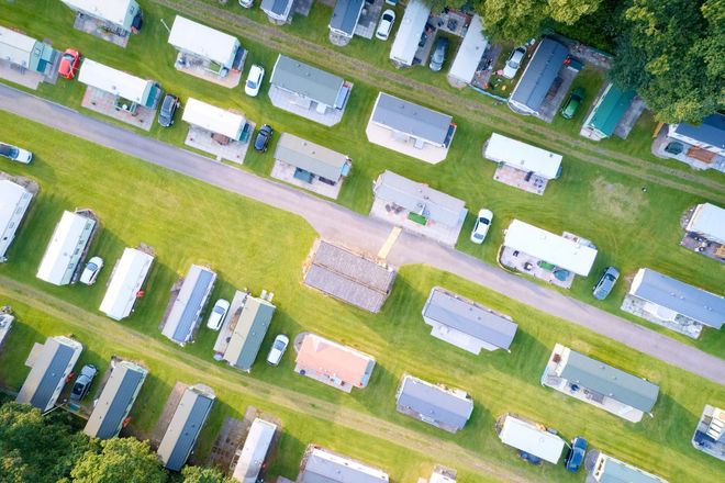 Aerial view of rows of white campers and trailers parked on green grass at a campground.