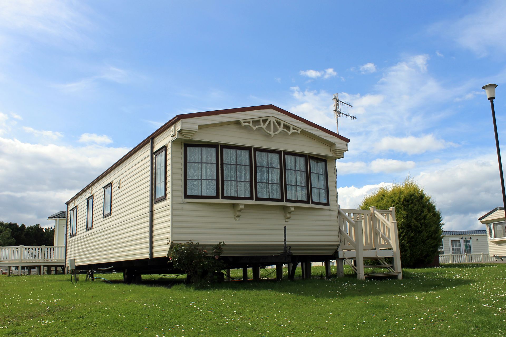 Small beige mobile home on grass under a blue sky with a porch and steps