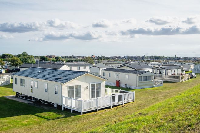 Rows of white mobile homes on a grassy hillside under a cloudy sky