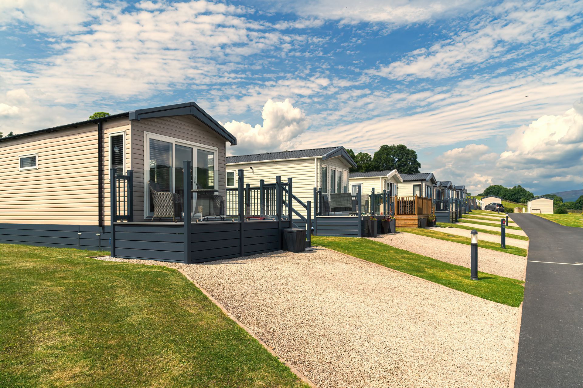 Row of modern mobile homes on a sunny paved park road with grassy lawns and gravel paths