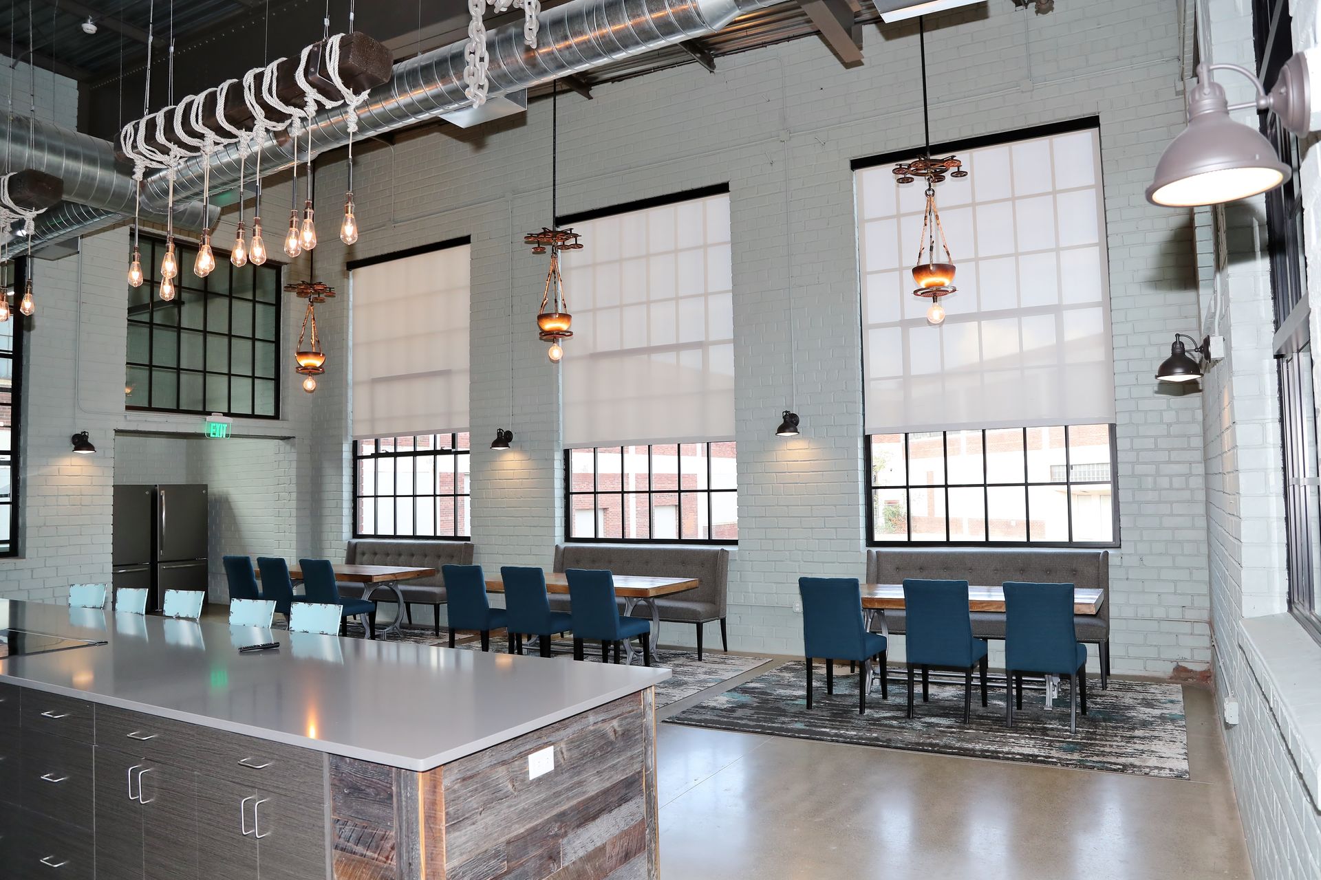 Modern dining area with large windows, industrial-style lighting, tables, chairs, and a large island.