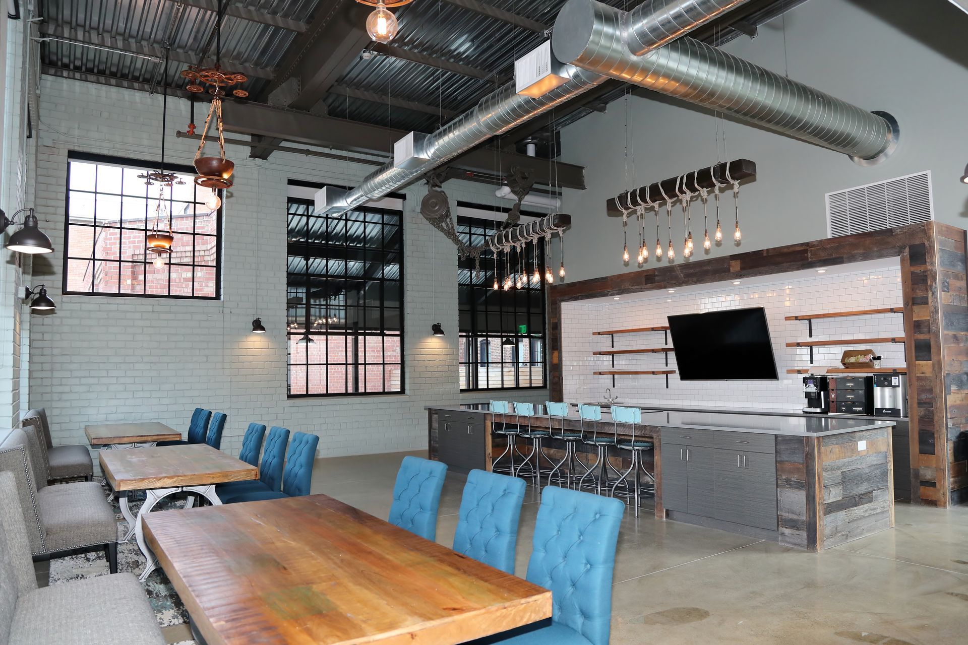 Modern industrial-style interior with tables, blue chairs, a large island, and exposed ductwork.