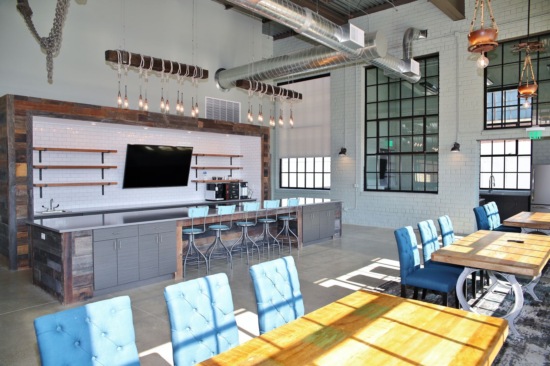 Modern lounge with tables, chairs, bar area, TV, and large windows.