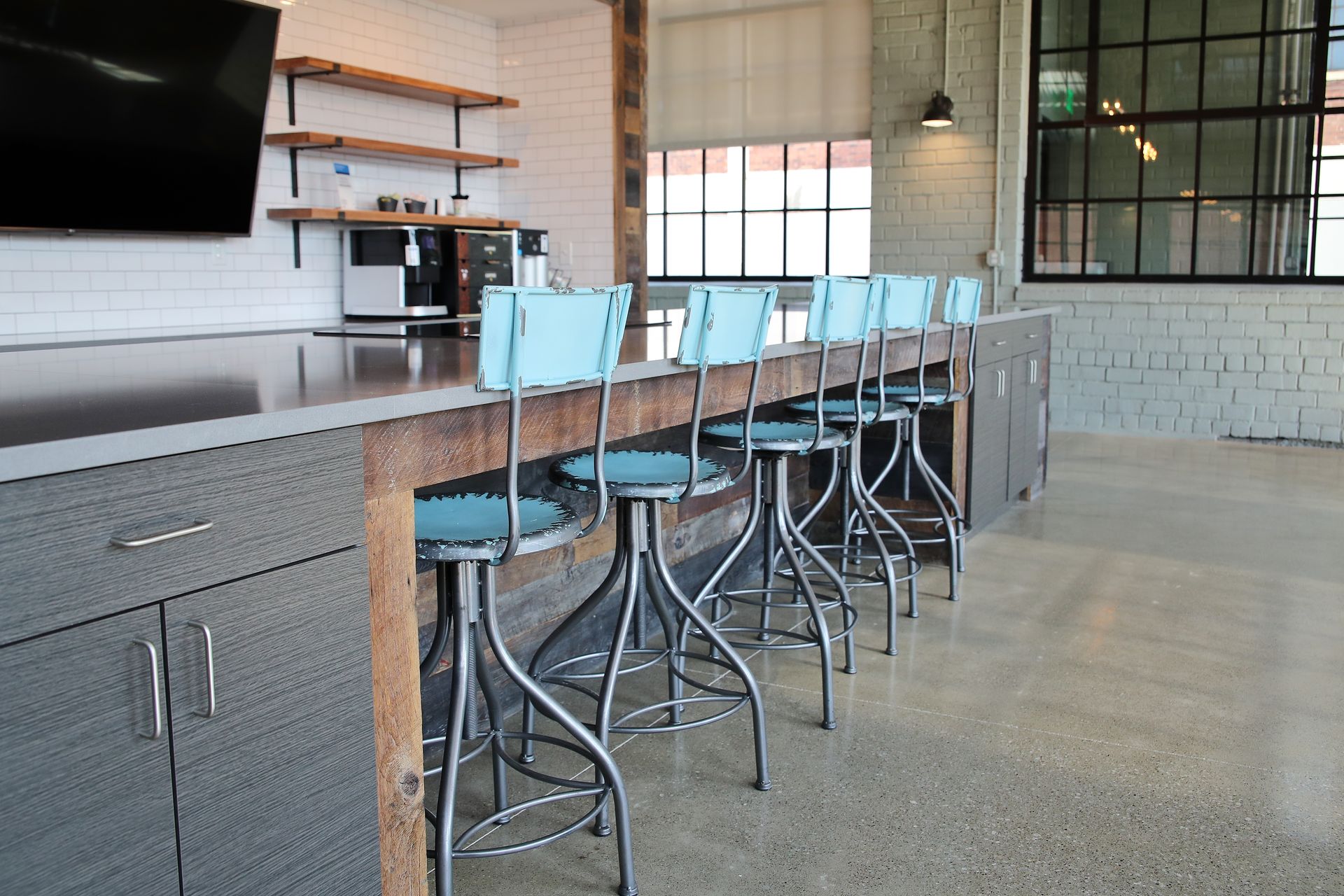 Modern kitchen area with counter and bar stools. Light blue stools, gray cabinets, and exposed brick.