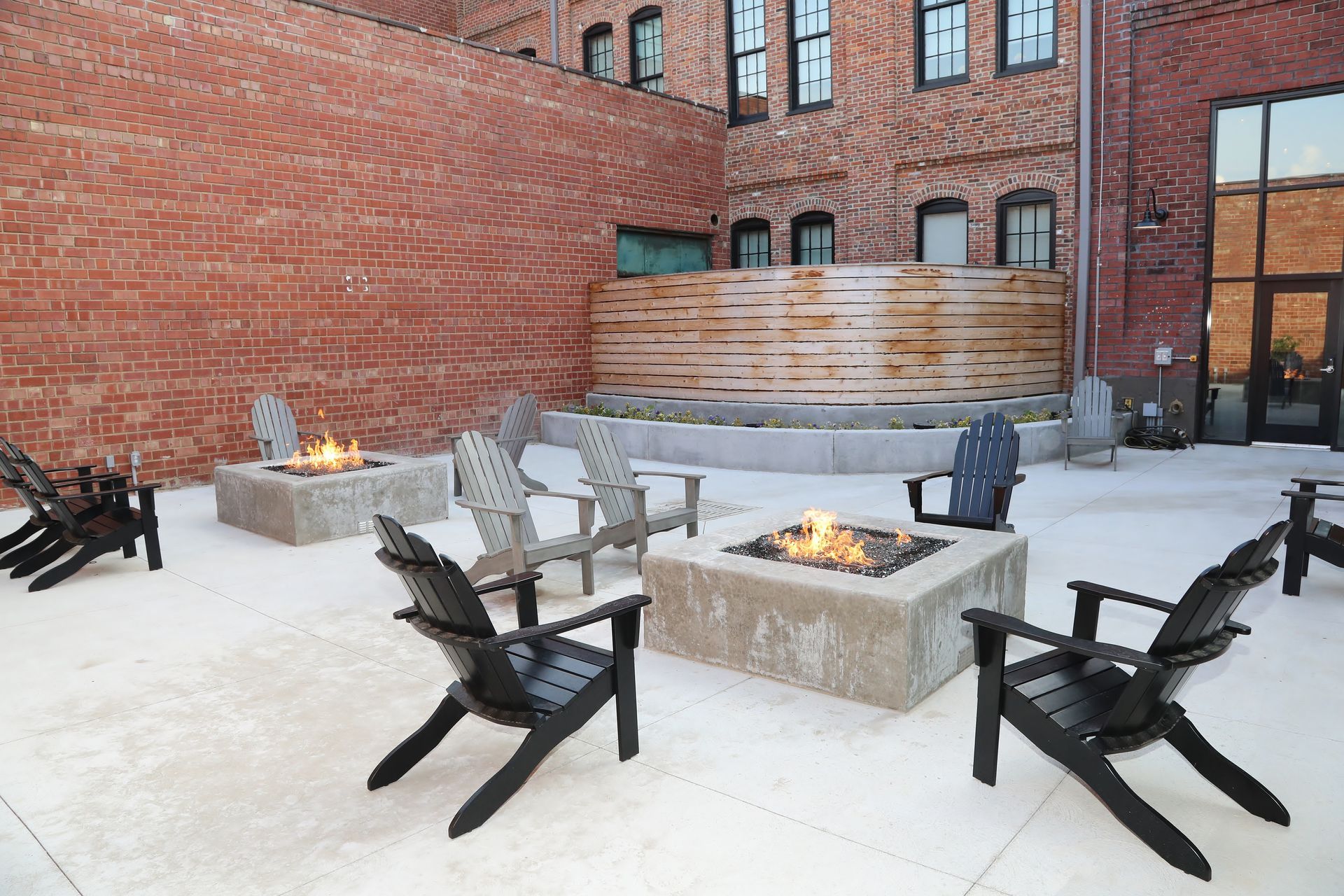 Outdoor patio with fire pits, Adirondack chairs, and a brick building backdrop.