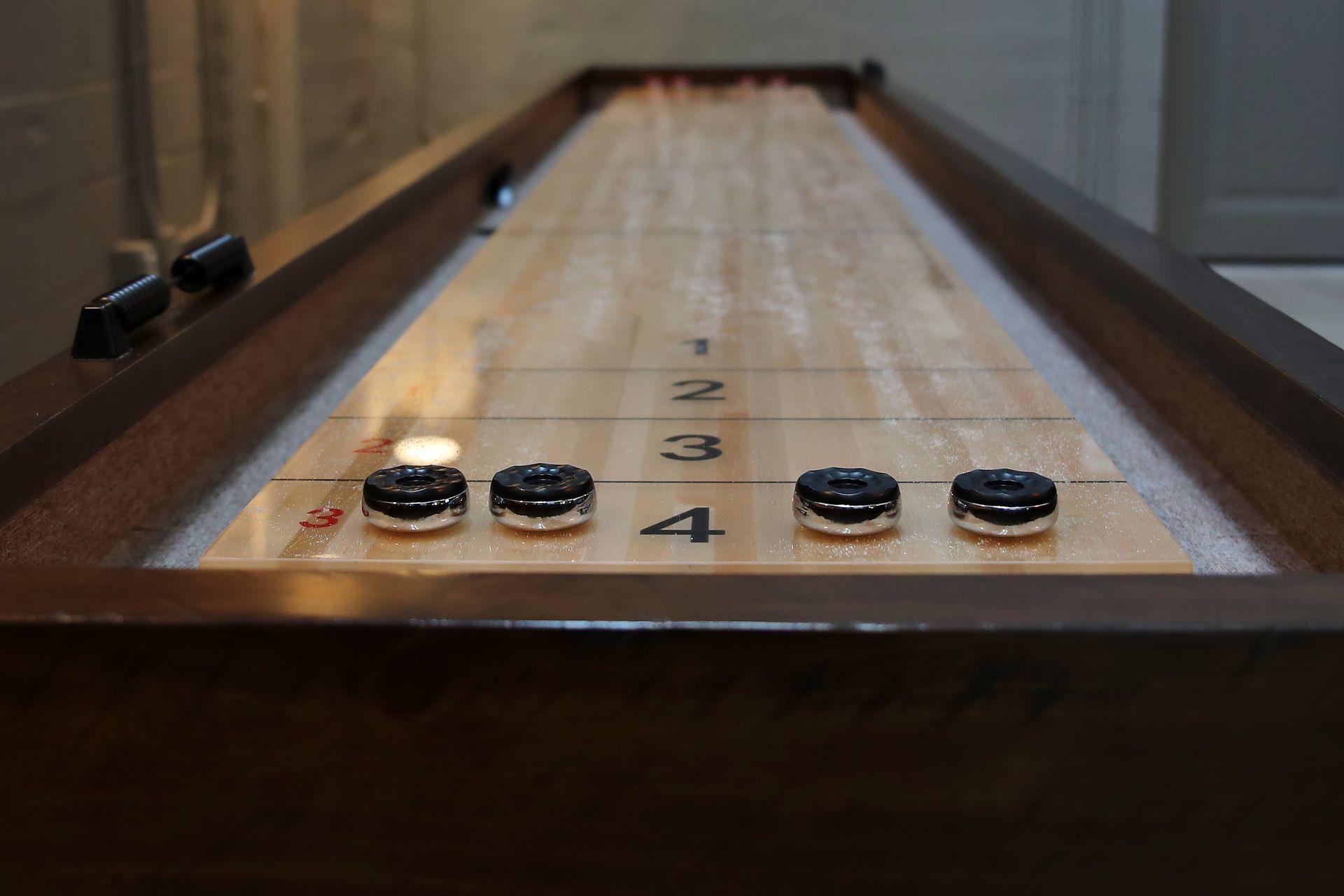 Shuffleboard table with pucks near the scoring end. Wooden surface, dark frame.