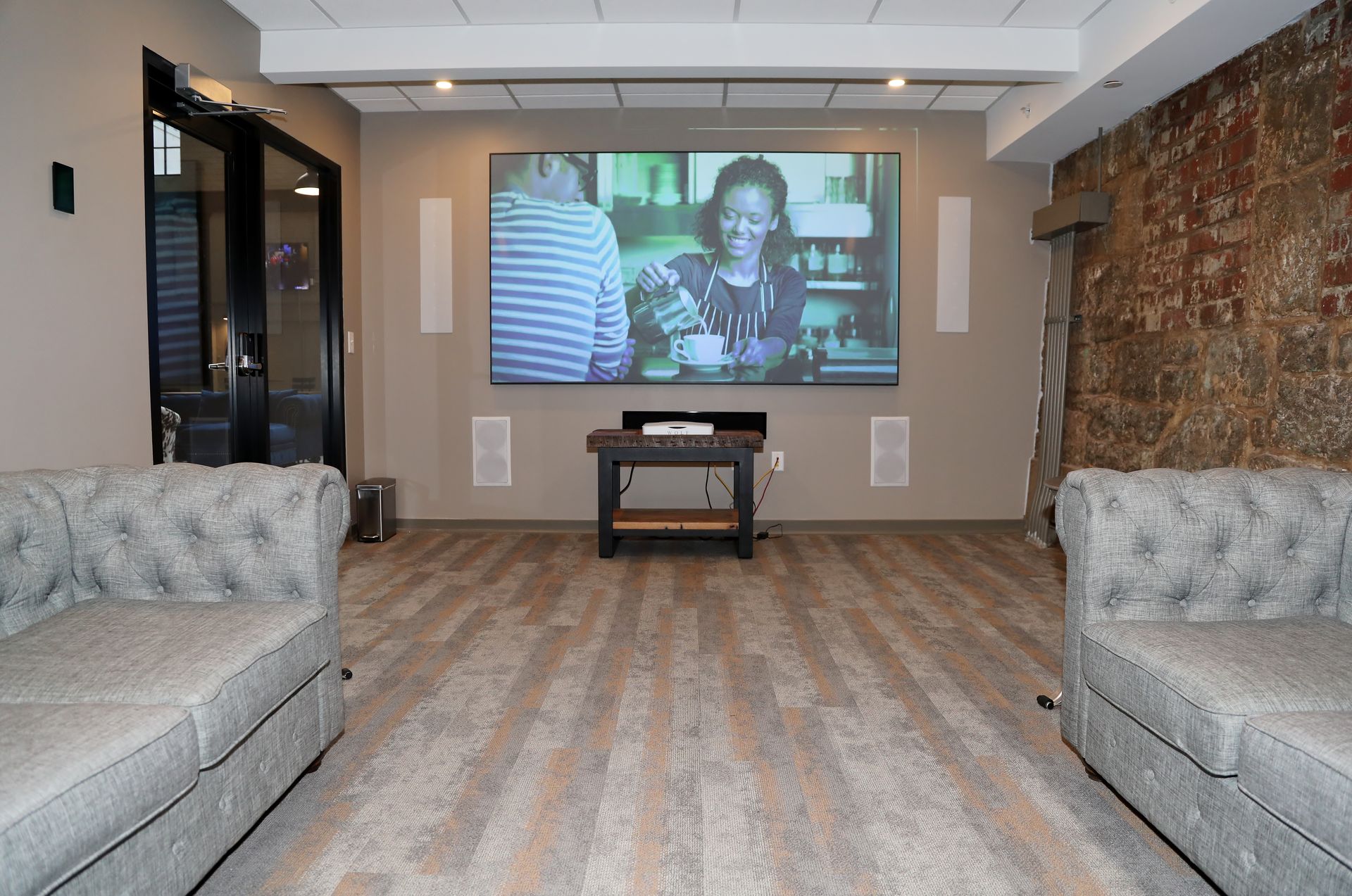 Home theater room: projector screen, sofas, wooden floor, brick wall.
